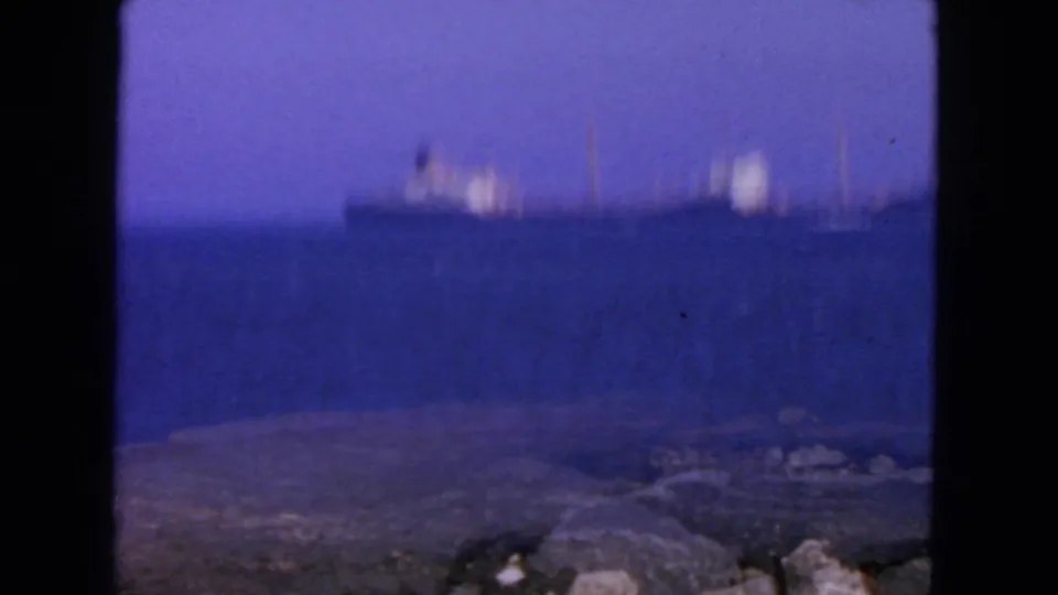Soft 8mm frame with a distant ship beyond blue water and a low rocky shoreline, consistent with the San Francisco coastal setting.