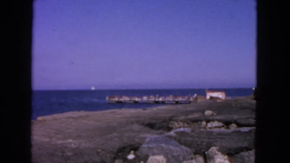 1963 San Francisco 8mm view of a rocky waterfront, low pier, small structure, and open blue water.