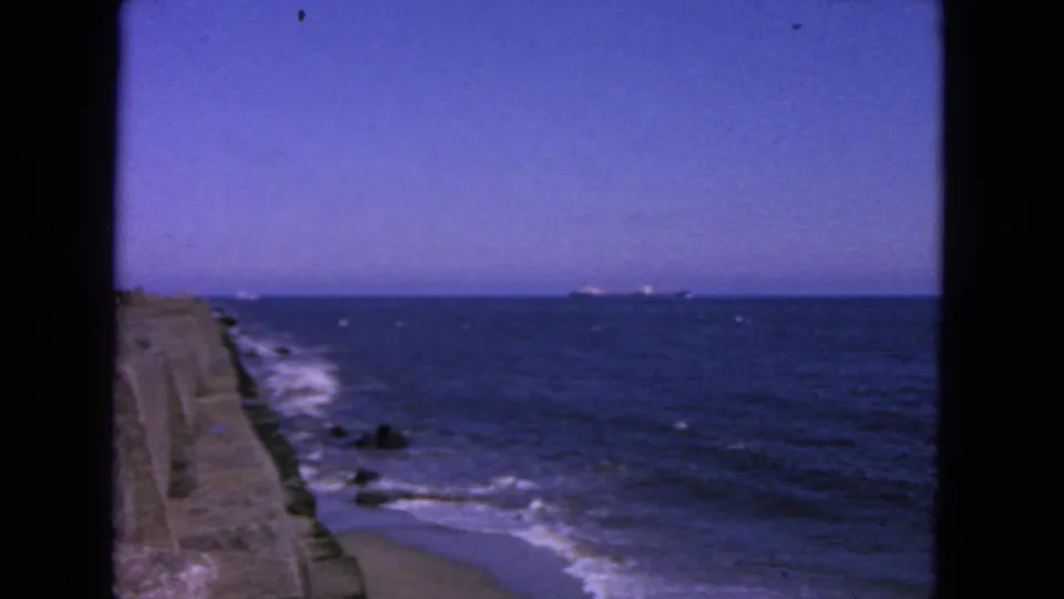 1963 San Francisco coastal frame showing a seawall, small waves, dark rocks, open water, and distant horizon.