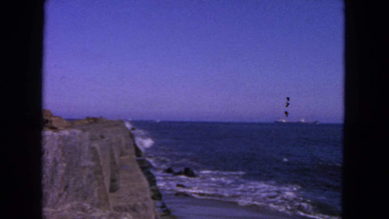Ocean view from a stone pier with waves and a distant vessel near the horizon.