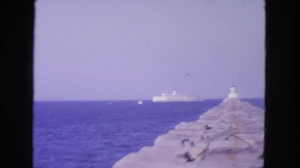 1963 San Francisco pier view with a long stone jetty, small beacon structure, and large white ship offshore.