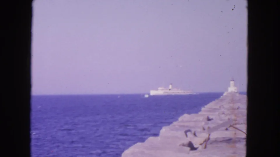 San Francisco 8mm frame from 1963 showing a stone jetty, small beacon, and distant ship across calm blue water.