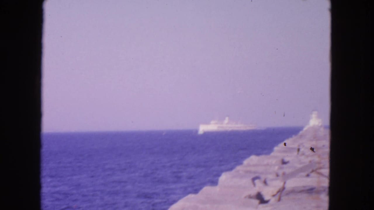 White passenger ship offshore beyond a rocky coast and dark window frame.