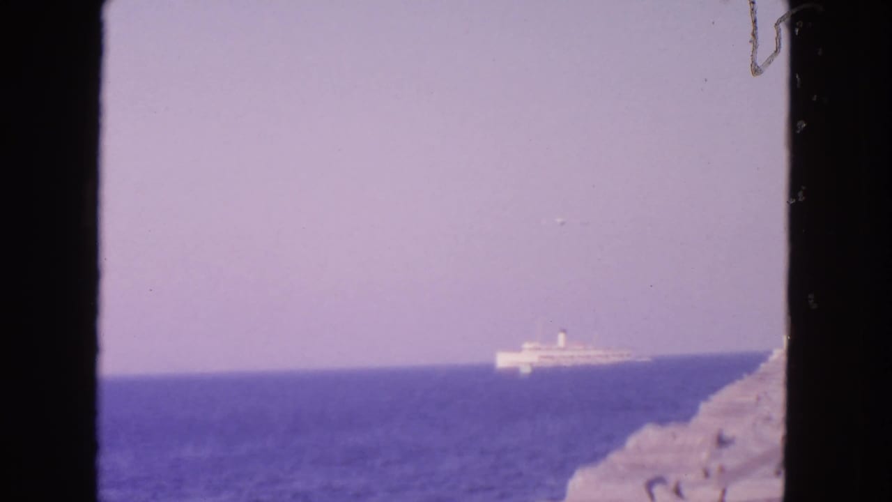 Distant white ship on blue water with rocky shoreline at the right edge.