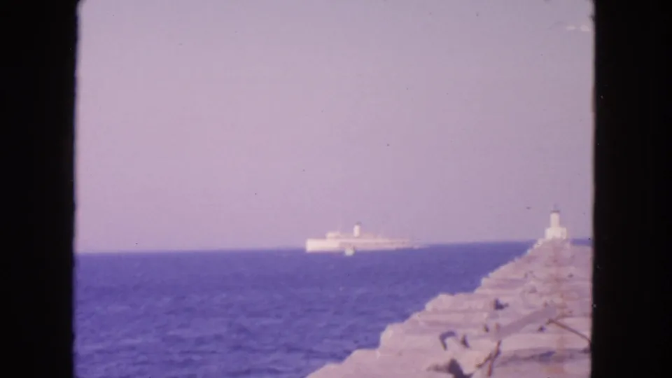 The 8mm frame shows a rocky pier or breakwater with a small beacon and a white ship farther out on the water.