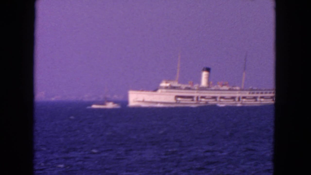 White passenger ship on blue open water under a hazy sky, with a small boat nearby.