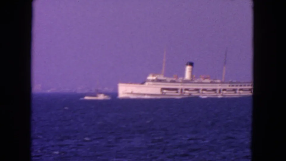 1963 San Francisco-area 8mm frame showing a distant white passenger ship on open water with a small boat at left.