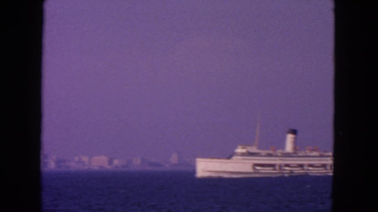 White passenger ship crossing blue water with a hazy distant skyline and dark frame edges.