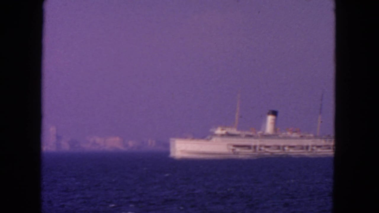 Passenger ship near the right side of the frame on blue water below a hazy skyline.