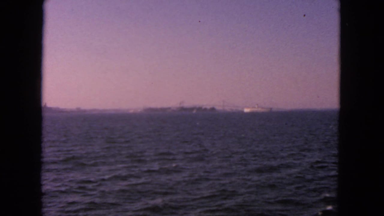 1963 San Francisco Bay home-movie frame showing open water, a distant ship, and a hazy horizon through dark frame borders.