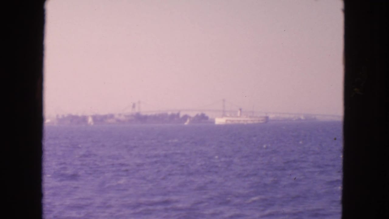 1963 8mm view from San Francisco Bay showing open water, hazy shoreline, and a distant suspension bridge.