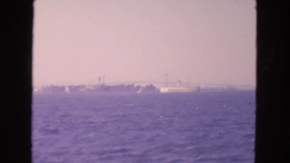 1963 8mm view from San Francisco Bay showing open water, hazy shoreline, and a distant suspension bridge.