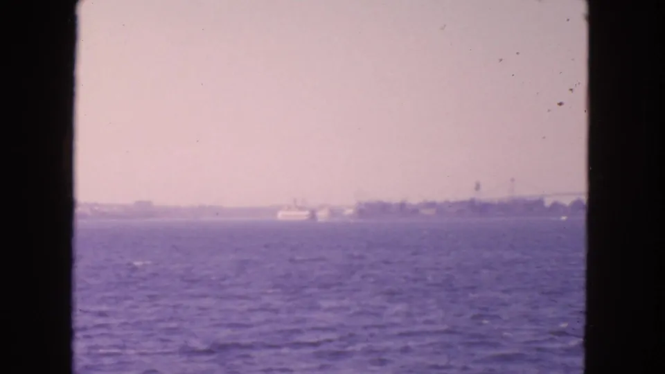 1963 San Francisco Bay view with a white ferry-like vessel crossing in front of a distant shoreline.
