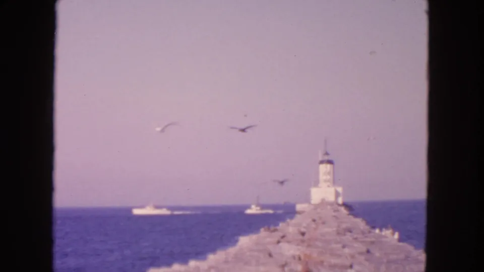 San Francisco 1963 home-movie view of a lighthouse on a breakwater, with gulls overhead and boats moving across the bay.