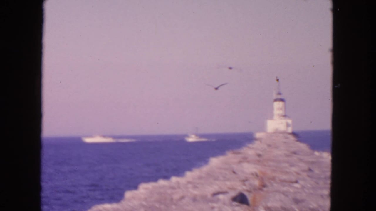 Lighthouse at the end of a rocky breakwater with boats on the sea.