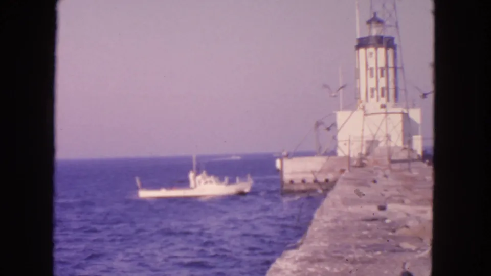 1963 San Francisco coastal footage shows a white lighthouse on a pier or breakwater with a small boat on the water.