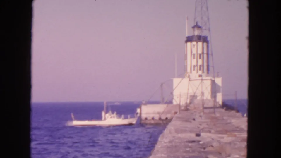 1963 San Francisco coastal view with a small boat in the foreground water and a white lighthouse on the breakwater.