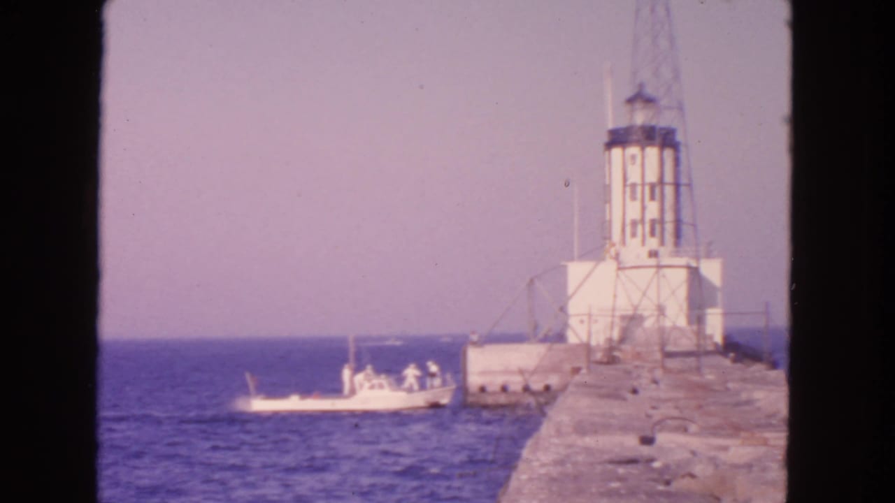Coast Guard boat near a lighthouse at the end of a concrete pier.