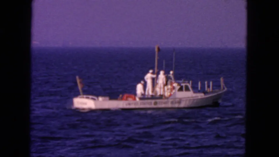 1963 San Francisco frame of a white Coast Guard-marked boat carrying uniformed crew across blue ocean water.
