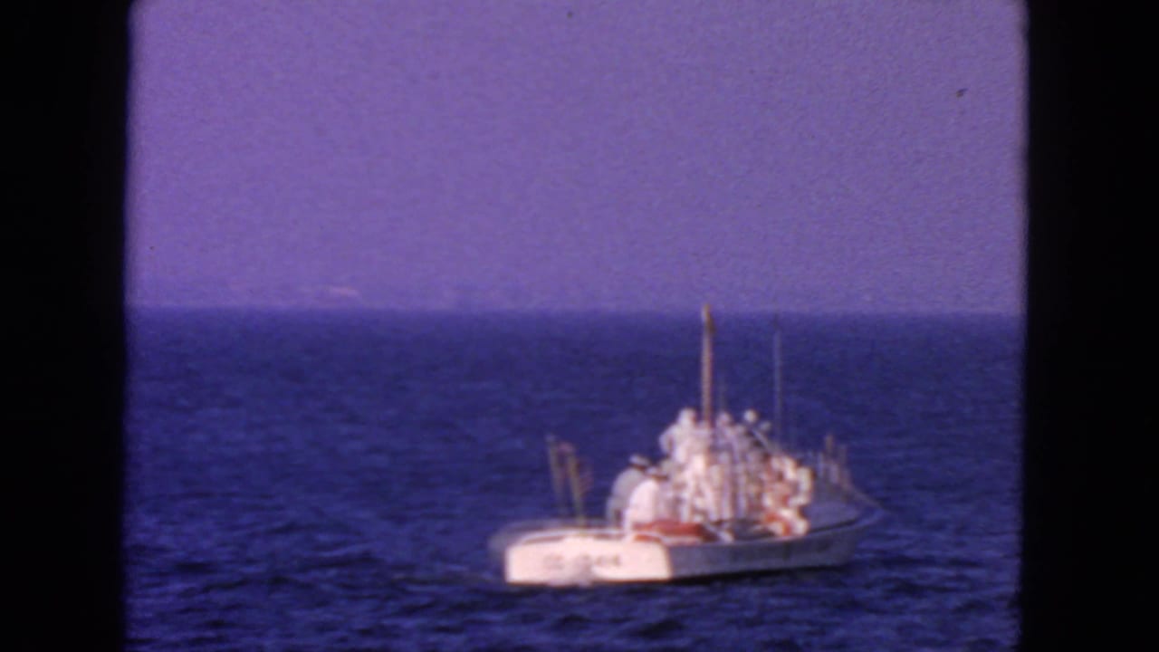 White Coast Guard boat seen from a distance on blue open water under a bright sky.
