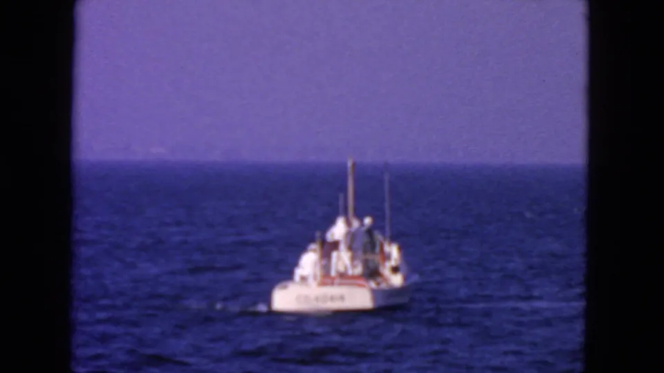 Distant 1963 coastal view of a white Coast Guard boat carrying crew on calm blue water.