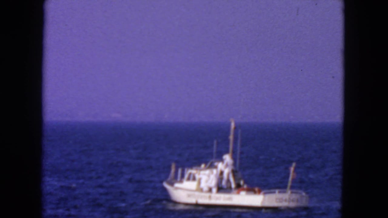 White Coast Guard boat moving across blue ocean under a purple sky.