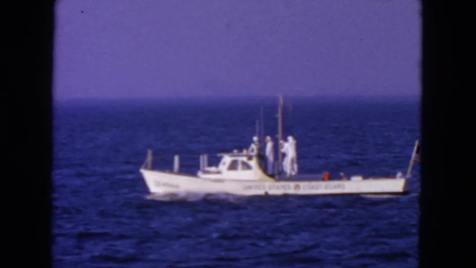 1963 San Francisco-area frame showing a marked United States Coast Guard boat with crew and a small American flag at sea.