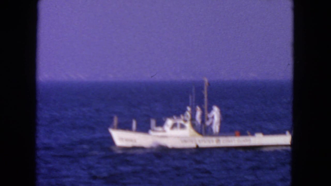 Small white Coast Guard boat moving across open blue water under a hazy sky.