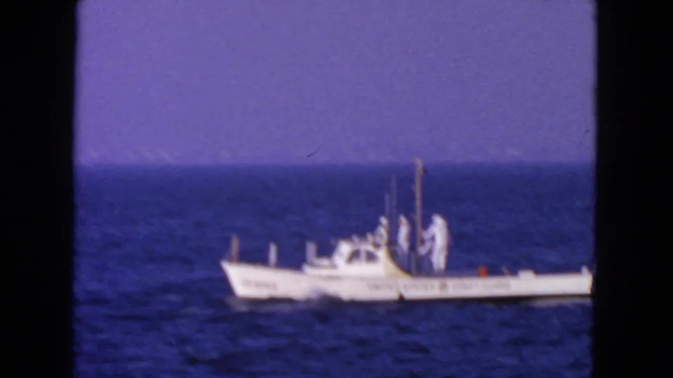Distant 1963 San Francisco 8mm view of a small white Coast Guard boat with crew visible on open water.