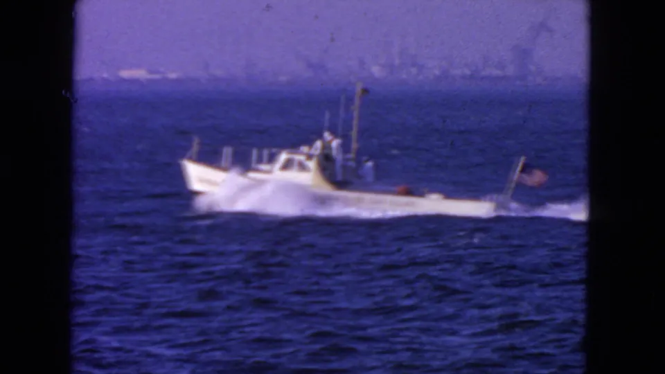 White speedboat with a small American flag travels across choppy water in 1963 San Francisco-area home-movie footage.