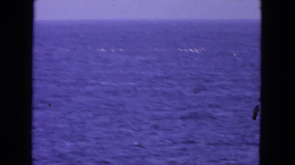 Open blue water fills the frame with small white wakes in the distance and dark 8mm film borders at the sides.