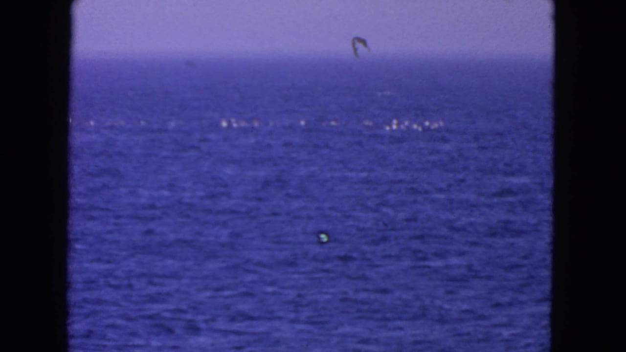 Blue ocean surface with a pale horizon and small white foam streaks, framed by dark film borders.