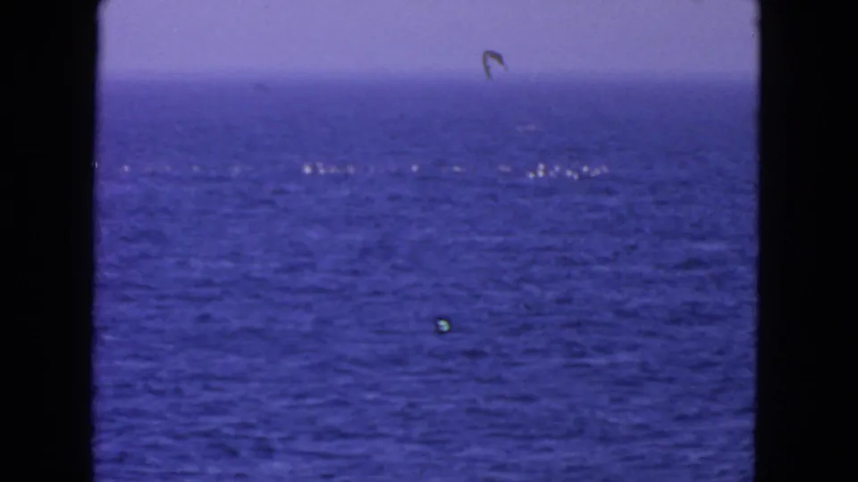 1963 8mm San Francisco-area ocean view with blue water, pale sky, scattered white foam, and visible film-gate borders.