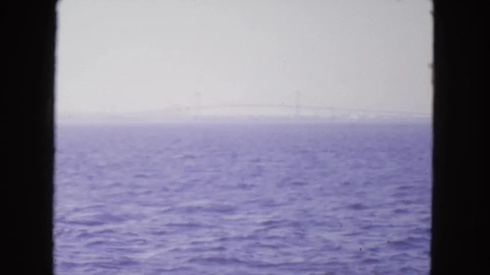 A 1963 San Francisco Bay boat-view frame shows rippled water and a faint suspension bridge through haze and dark window-like edges.