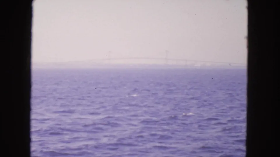 1963 home-movie footage from San Francisco Bay shows choppy water and a barely visible bridge line under a pale sky.