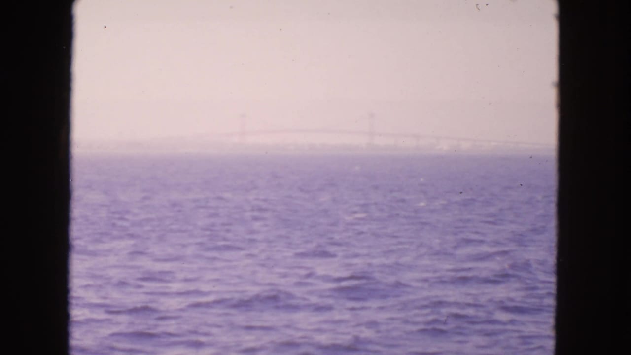 Hazy bay water seen through dark vertical frame edges with a faint bridge on the horizon.