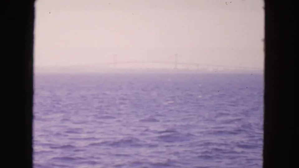 1963 San Francisco-area bay view with purple-blue water, haze, dark frame edges, and a faint distant bridge line.