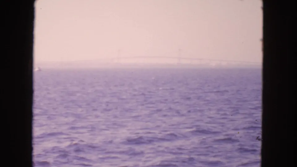 Soft 8mm view across San Francisco bay water with haze, purple color fading, and a distant suspension bridge barely visible.