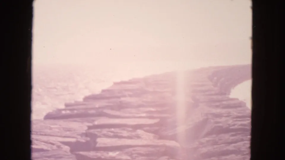 Vintage 8mm San Francisco shoreline view with a curved rock breakwater, bright ocean surface, and faded color.