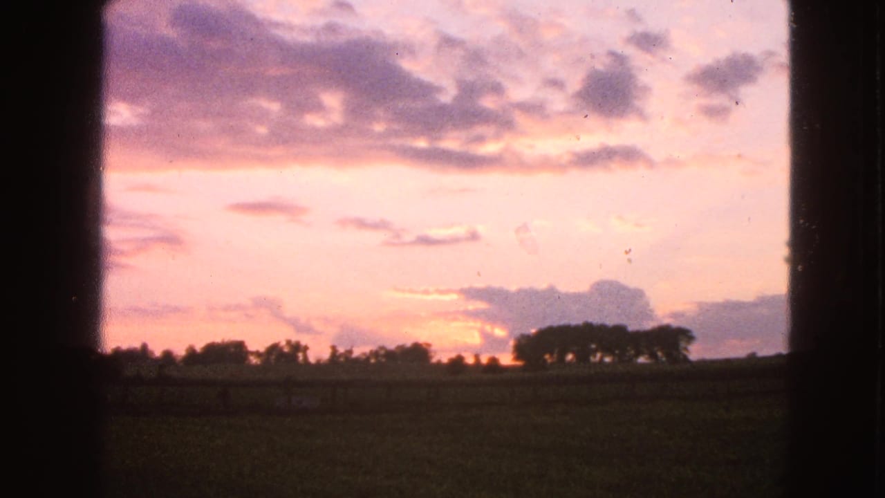 Walworth, Wisconsin home-movie frame with pastel sunset clouds above a field and silhouetted tree line in the distance.