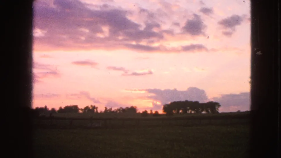1963 8mm countryside view in Walworth, Wisconsin, showing a glowing sunset behind distant trees and a dark open field.