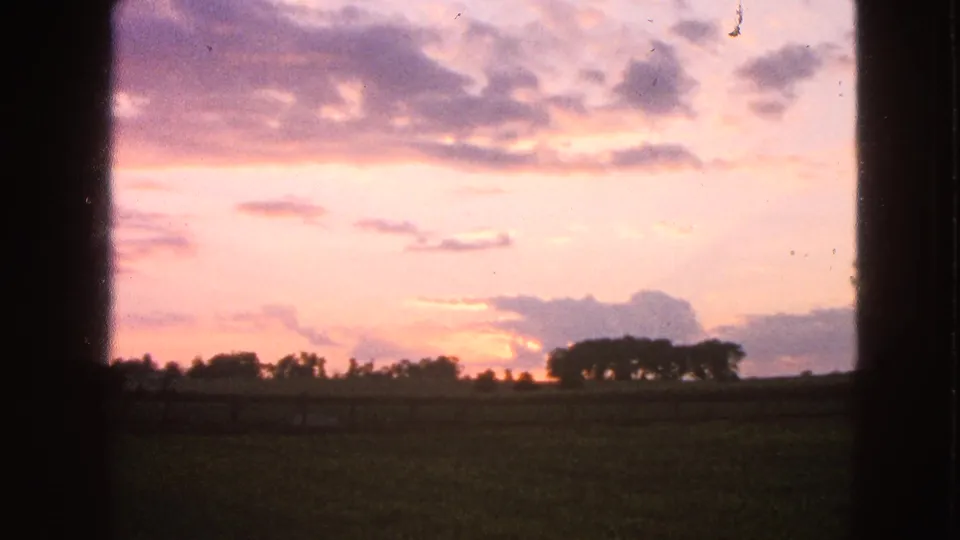 Final 8mm frame of the Walworth rural sunset, with pink clouds, a low treeline, dark field, and visible film texture.
