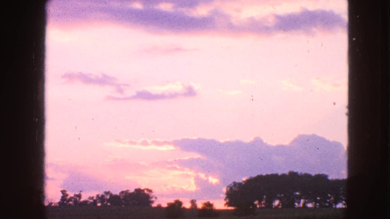 Lavender and pink clouds above a low silhouetted treeline at dusk.