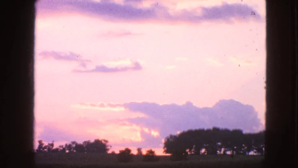 8mm home-movie frame of a pastel Wisconsin sunset, showing clouds and a dark treeline across the lower edge.