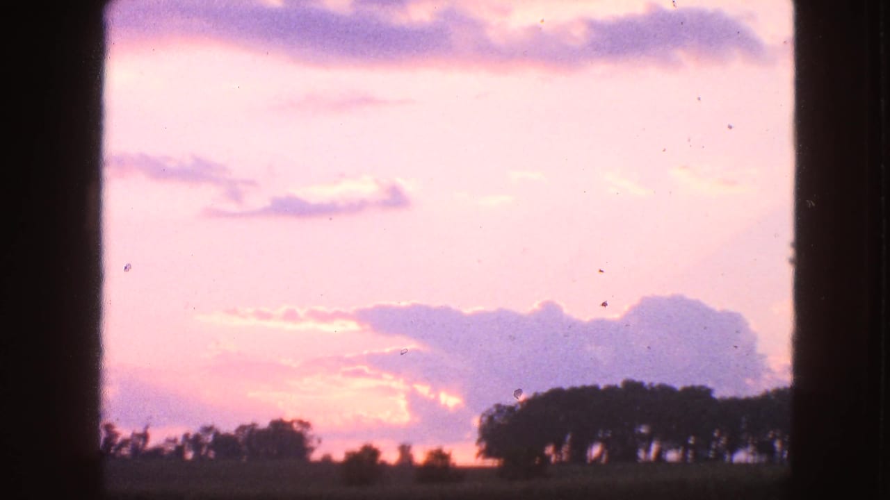 1963 Walworth, Wisconsin 8mm frame showing a pastel sunset sky, purple clouds, and silhouetted trees on a low horizon.