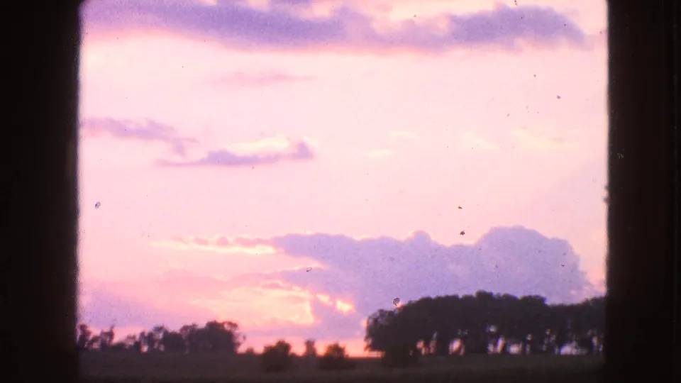 1963 Walworth, Wisconsin 8mm frame showing a pastel sunset sky, purple clouds, and silhouetted trees on a low horizon.