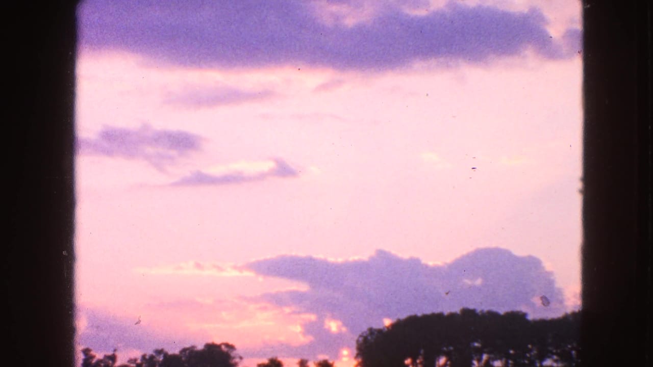 Walworth, Wisconsin home-movie frame with a soft pink sky, purple clouds, low sun glow, and dark trees along the horizon.