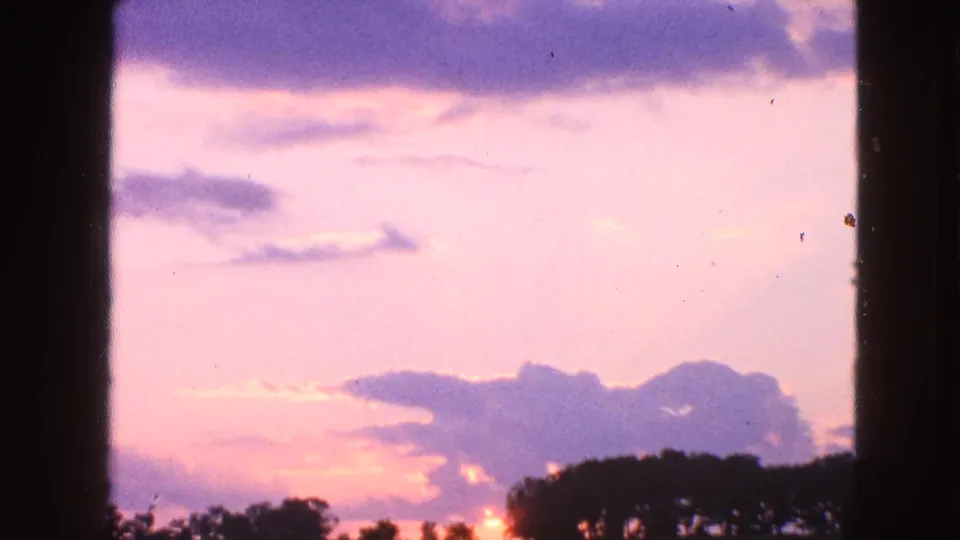 1963 8mm frame from Walworth, Wisconsin showing a pastel evening sky and silhouetted trees beneath broad purple clouds.