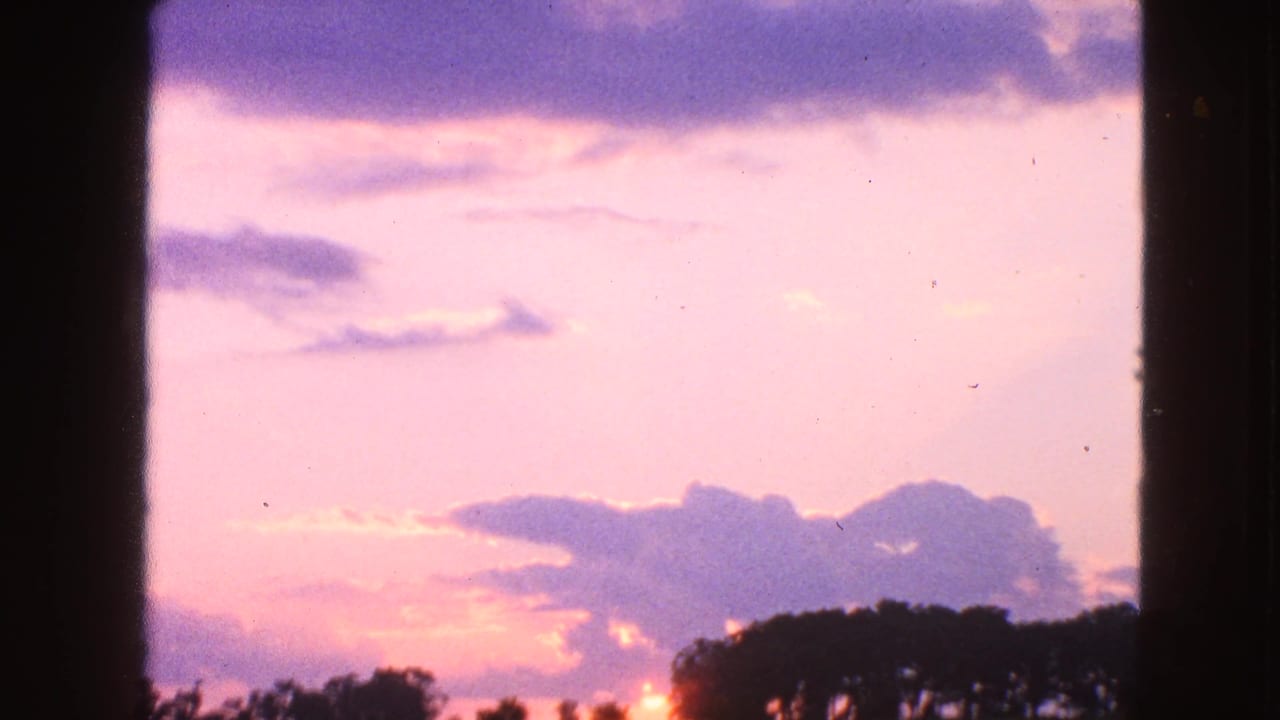 Pink sunset sky and clouds seen through dark window panes with trees along the lower edge.