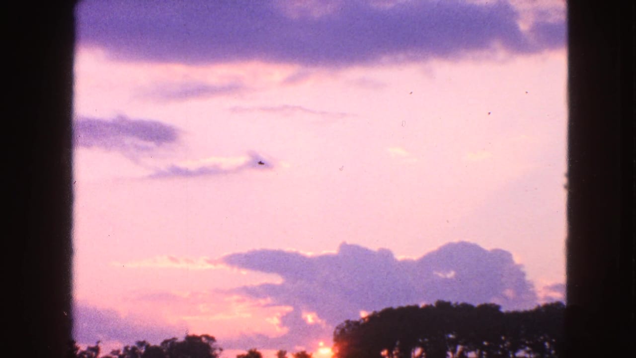 1963 Walworth, Wisconsin 8mm view of a sunset sky through a window, with clouds above a dark treeline.